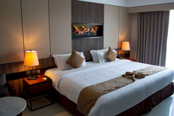 A cozy hotel room features a large bed with pillows, bedside lamps, and curtains, creating a warm and inviting atmosphere.