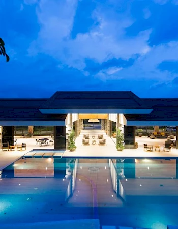A luxurious modern building with a large, illuminated pool in the foreground under a twilight sky.