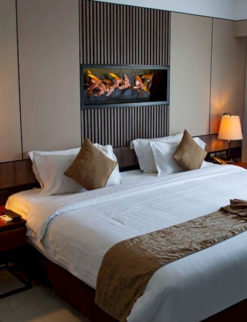 A modern hotel room with a large bed, decorative pillows, bedside tables, lamps, and wall art above the headboard.