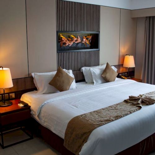 A well-furnished hotel room with a large bed, decorative pillows, bedside lamps, and curtains, creating a cozy and elegant atmosphere.