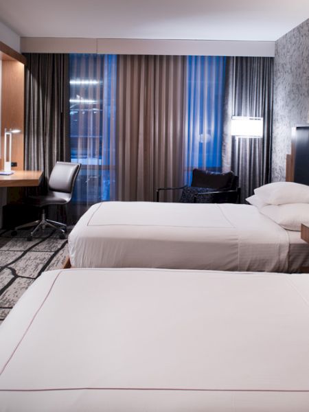 A modern hotel room with two beds, a desk, a large TV, and stylish lighting and decor.
