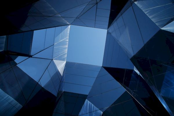 Geometric glass structures form a kaleidoscopic pattern, creating a blue sky opening at the top center of the image.