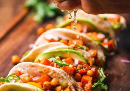 A hand is squeezing lime over tacos filled with chickpeas, avocado, onions, and cilantro. Lime slices are placed in front on a wooden surface.