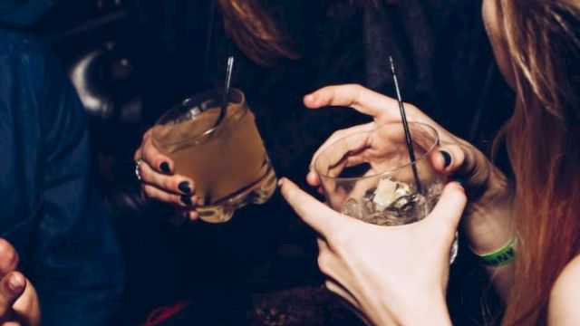 People are enjoying drinks and laughing in a lively setting, showing a close interaction and festive atmosphere.