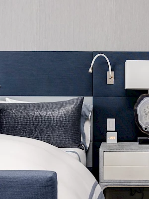 A modern bedroom with a navy bed and headboard, nightstand, lamp, and decorative pillow accents the space.
