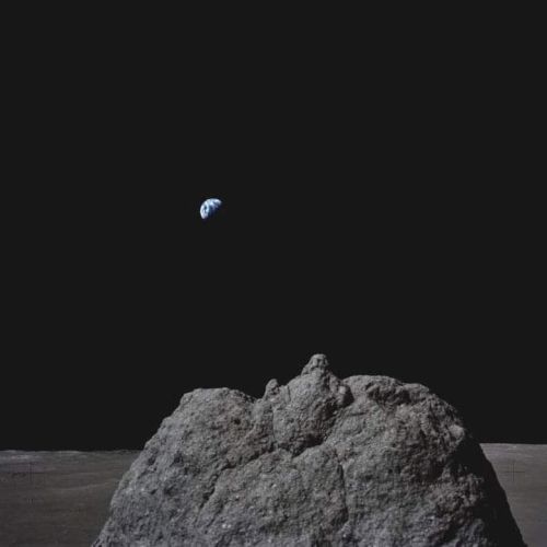 A rocky lunar surface with Earth visible in the dark sky above.