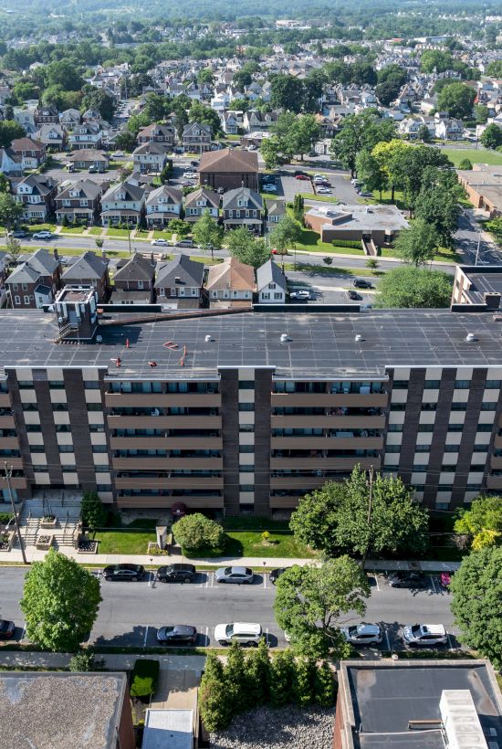 Aerial view of a large rectangular building in a suburban area, surrounded by trees, smaller houses, and roads ending the sentence.