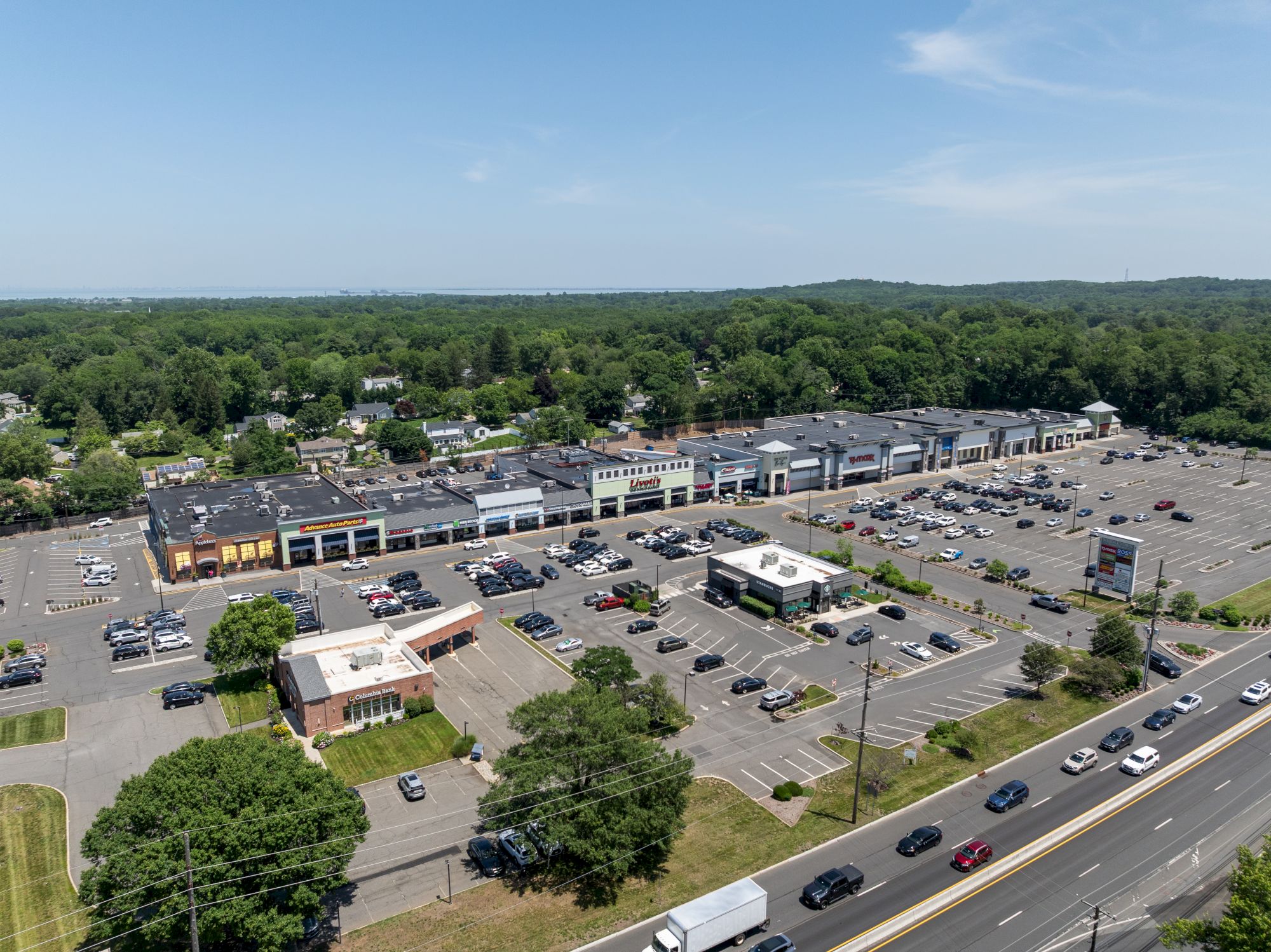 An aerial view of a shopping plaza with multiple stores, a large parking lot, and a road with cars in front.