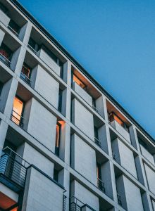 A modern building with balconies and warm lights seen against a clear blue sky, viewed from a low angle.