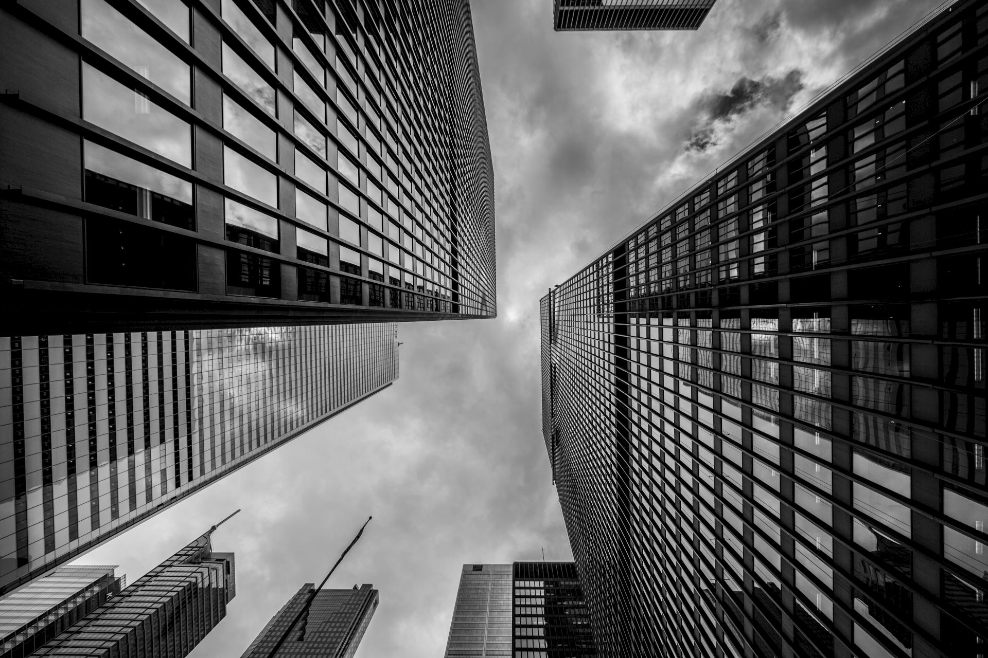 A black and white photo looking up at skyscrapers with reflective windows against a cloudy sky.