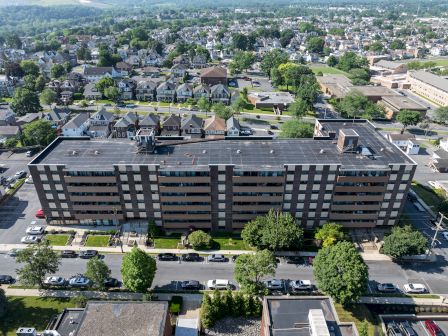 An aerial view of a large, multi-story building with a flat roof, surrounded by residential homes and trees in a neighborhood setting.
