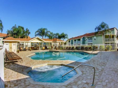 A serene outdoor pool and hot tub area surrounded by lounge chairs and buildings, under a clear blue sky and palm trees.