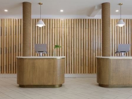 A modern reception area with two wooden desks, laptops, pendant lights, and a slatted wood wall in the background, creating a minimalist look.