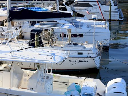 The image shows several docked boats with one named "Good Stories," featuring a calm water setting and nautical equipment on board.
