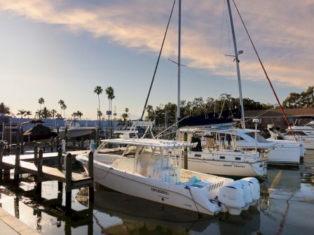 A marina with several docked boats, calm waters, and a clear sky with scattered clouds.