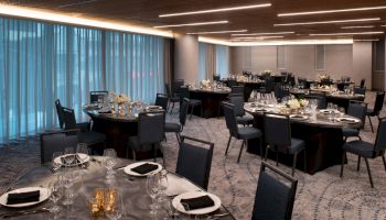 The image shows an elegantly set banquet room with round tables, chairs, and formal dinner settings, under warm ceiling lighting.