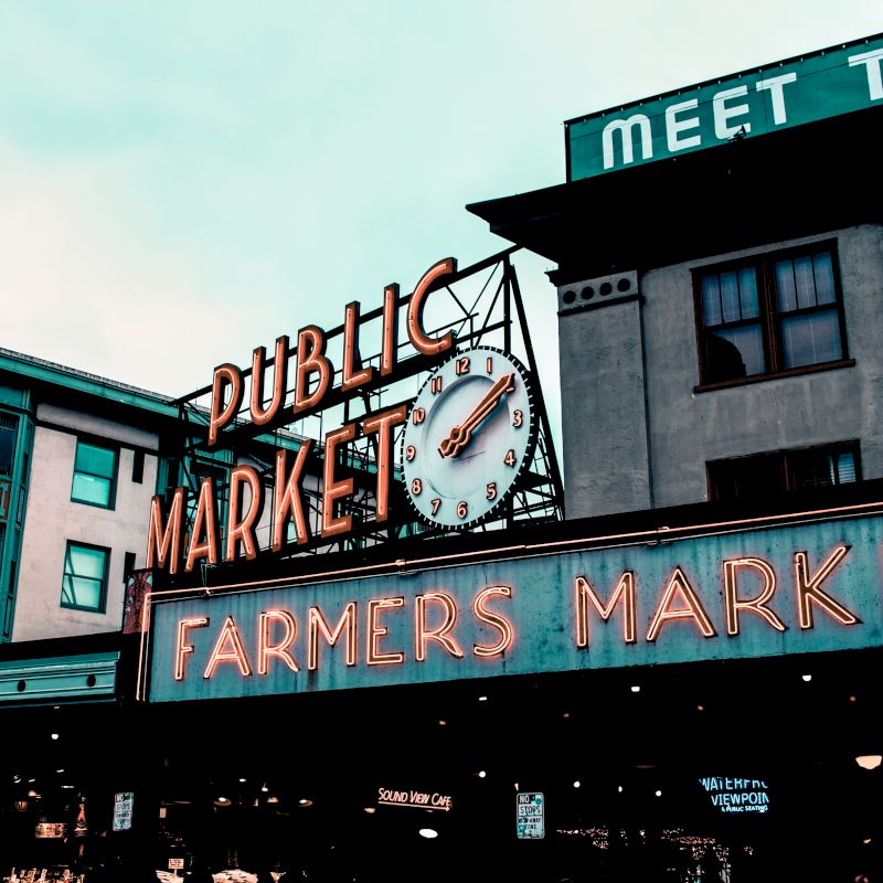 The image features the iconic signage of a public market and farmers market, with a clock, set against a backdrop of buildings.