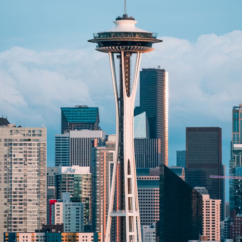 The image shows a city skyline with the Space Needle prominently in the foreground against a backdrop of various modern buildings.