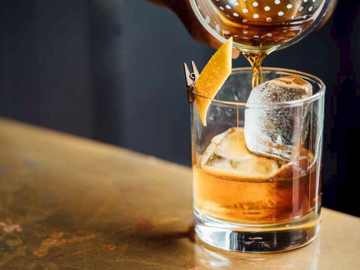 A cocktail being poured over ice into a glass with a garnish, possibly a twist of citrus.