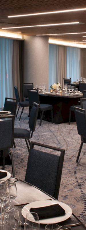 A banquet room with round tables set elegantly for an event, featuring flowers and candles, beneath modern ceiling lights.