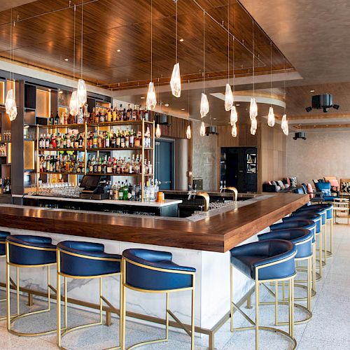 A modern bar with stylish seating, hanging lights, and a well-stocked counter is set in a spacious, stylish lounge area.