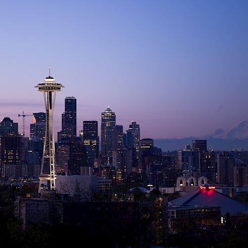 Seattle skyline at dusk with the Space Needle, city buildings, and Mount Rainier in the background.