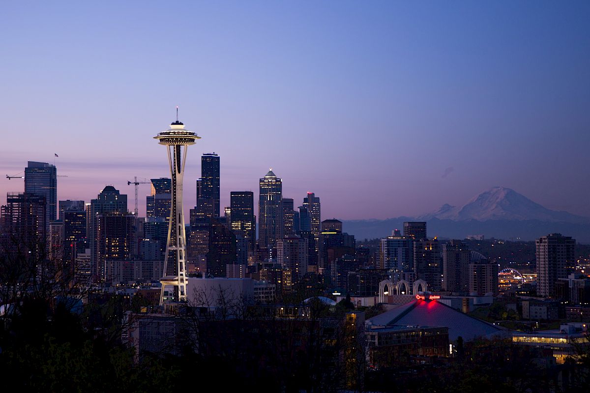 A scenic view of Seattle's skyline at dusk, featuring the Space Needle and Mount Rainier in the background.