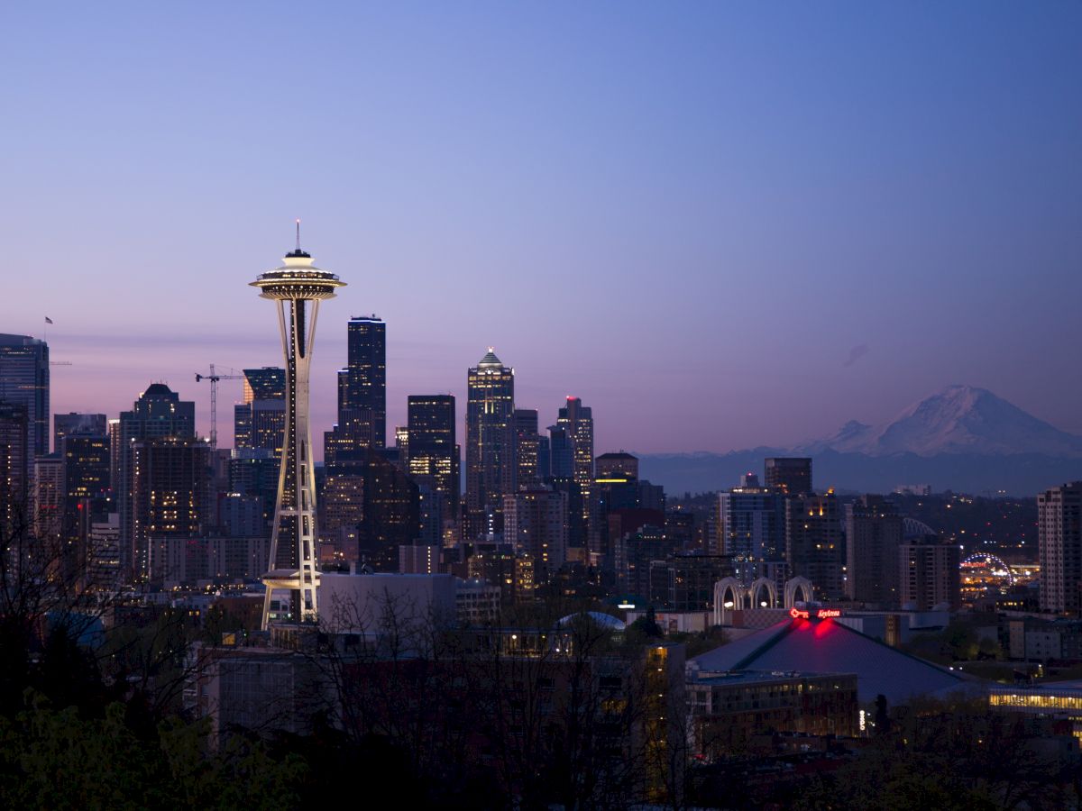 A scenic view of Seattle's skyline at dusk, featuring the Space Needle and Mount Rainier in the background.