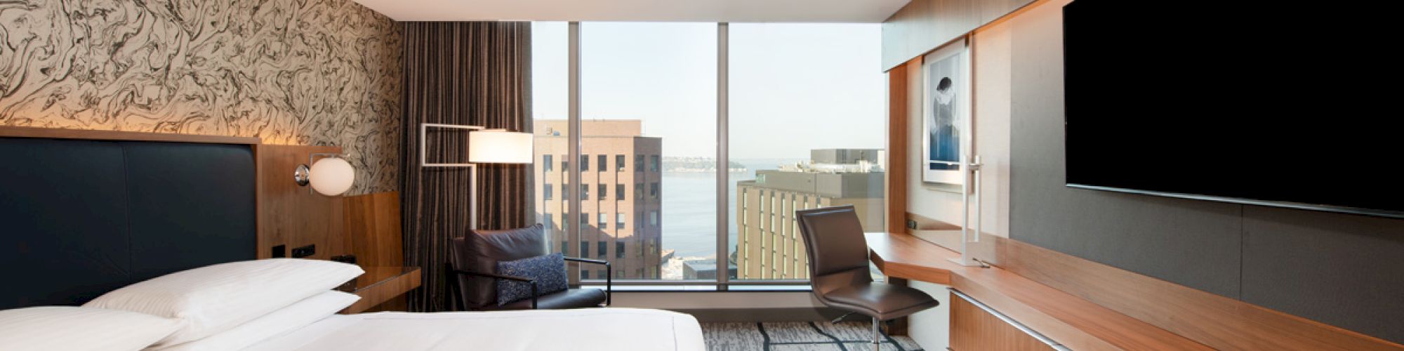 A modern hotel room with a large bed, a flat-screen TV, and a window view of the city skyline ending the sentence.